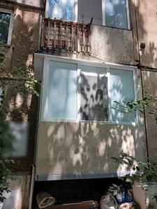 Balconul finalizat la parterul blocului, închis cu tâmplărie albă, sub balconul vechi de la etajul întâi